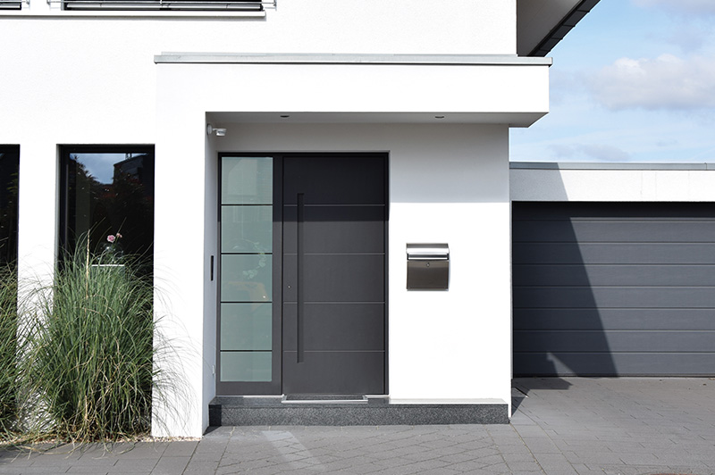 Moderner Hauseingang mit schwarzer Tür, seitlichem Glasfenster, Briefkasten und angrenzender Garage