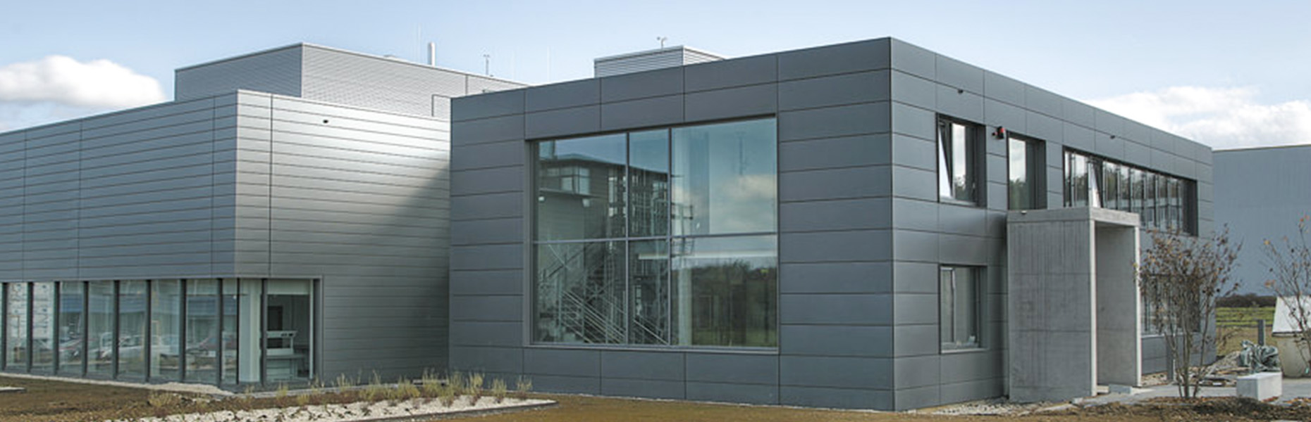 Modernes Bürogebäude mit großen Fenstern und grauer Fassade unter bewölktem Himmel