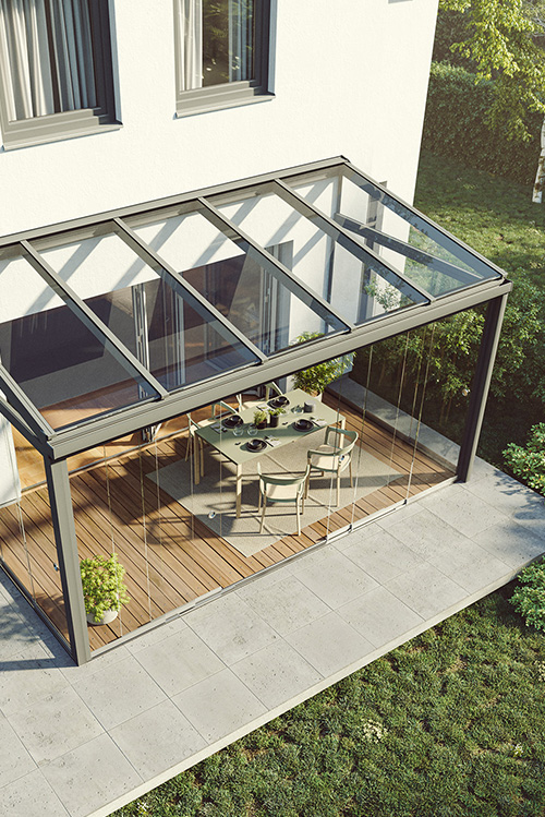 Modernes Einfamilienhaus mit Glas-Terrassendach und Sitzbereich mit Tisch und Stühlen auf Holzterrasse