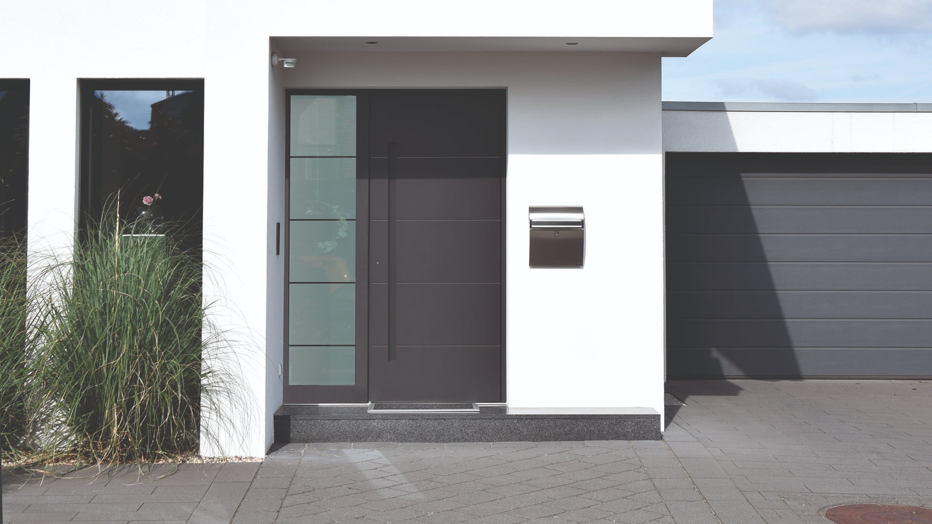 Moderner Hauseingang mit großer dunkler Tür, Glasfenster links, Briefkasten und angrenzender Garage