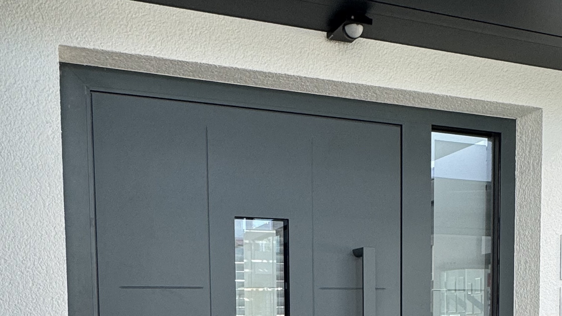 Moderne Haustür mit großem Griff und seitlichem Fenster, weißer Putzfassade