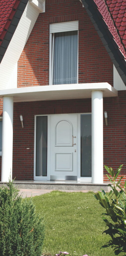 Eingang eines Hauses mit weißer Haustür, zwei seitlichen Glasfenstern und zwei weißen Säulen unter einem Giebel mit rotem Ziegeldach