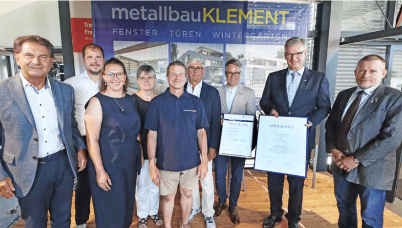 Gruppe von acht Personen steht vor einem Banner mit der Aufschrift 'Metallbau KLEMENT Fenster Türen Wintergärten', zwei Personen halten Urkunden