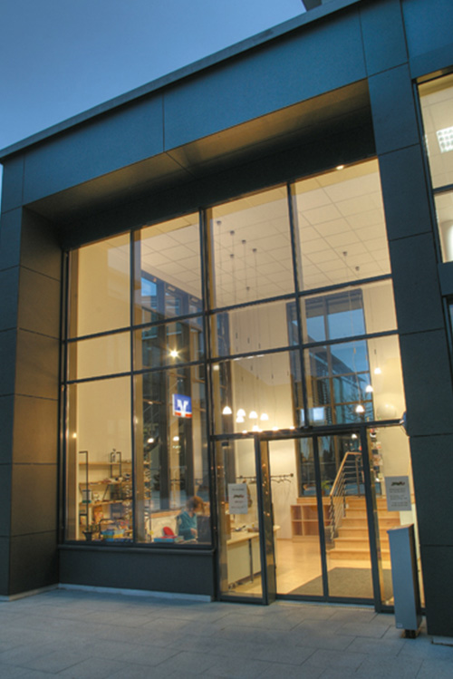 Große Glasfassade eines modernen Bürogebäudes mit Blick auf Innenraum und beleuchteter Treppe